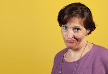 Incredulous attractive mature woman in purple blouse on a yellow background looking at the camera