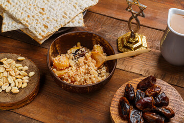 A plate of couscous with saffron and nuts on a wooden table next to matzah and a jug of fruit broth.