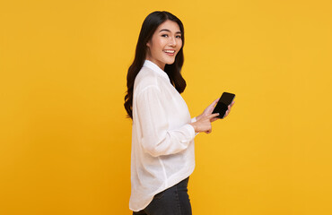 Happy young Asian woman showing at blank screen mobile phone isolated over yellow background.