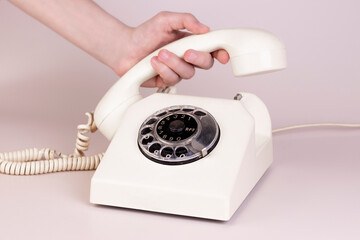 Minimal retro concept, girl hand answering vintage phone on light background. Retro telephone call aesthetic, promotion, communication.