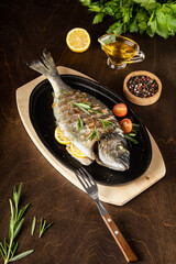 roasted dorado fish with lemon on dark wooden background. Copy space.Vertica