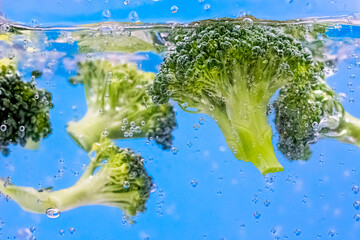 Freshness broccoli with water splash and bubbles on blue background. Close up image, selective focus.