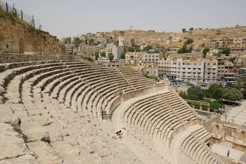 Ruins of an ancient Roman amphitheatre - the Odeon Theater in the city of Amman in Jordan. There are silhouettes of standing people.