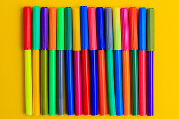 Multi-colored markers with mixed caps. Creative concept. Yellow background with selective focus and...