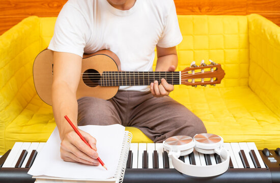 male amateur songwriter writing a hit song on white paper while playing acoustic guitar in living room. song writing concept