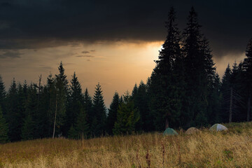 Mountain landscape at dramatic sunset. Tourist tents near forest.