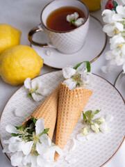 Fototapeta na wymiar White tea set with tea in cups with yellow lemons and a blossoming apple branch.View from aboveThere are waffle cones on a saucer.