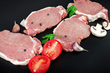 Pieces of raw roast beef meat with parsley, garlic, champignons, tomato on dark background