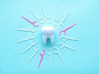 Dental concept of oral hygiene. Dental floss with a white and pink plastic toothpick lie in a circle in the center of a large white tooth