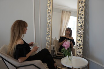 In the photo, a beautiful girl in a black dress, long hair and bangs looks in the mirror and sees...