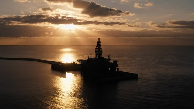 Offshore oil and gas platform aerial view. Silhouette of drilling rig (jack up rig) in sea or ocean at sunrise. Offshore exploration of crude oil and gas. Petroleum and chemical industry concept
