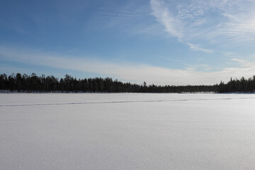 frozen lake with green forest and blue sky, incredible finnish lapland winter landscape