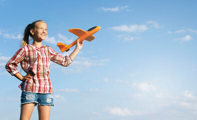 A girl with a toy airplane in her hand against a blue sky background. Happy childhood. Summer vacation. Journeys.