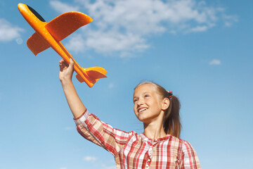 A girl with a toy airplane in her hand against a blue sky background. Happy childhood. Summer vacation. Journeys.