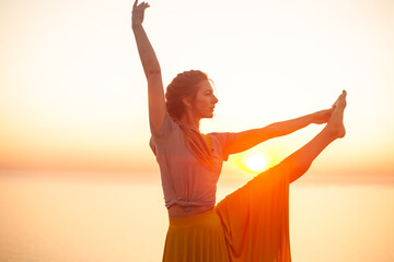 Plakat Back view of young woman engaged in yoga in nature with view and warm light of sunset, makes poses enjoy the meditation, balance and sunrise