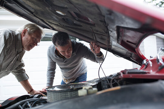 Two Men Looking Under Hood Of Car On Driveway