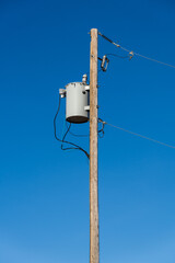 An isolated power pole with working utilities and a transformer against a blue sky in Rocky View...