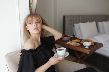 In the photo, the girl is drinking coffee at her balcony. A man takes a picture of her, she is enjoying the morning and breakfast