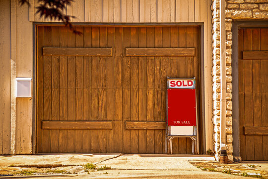 Two Car Garage With Rustic Wooden Doors With For Sale Sign Saying Sold Propped Up Against It - Copy Space