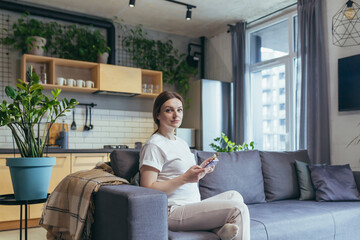 Obraz premium Pregnant woman sitting on sofa at home using phone for online shopping, holding a bank credit card