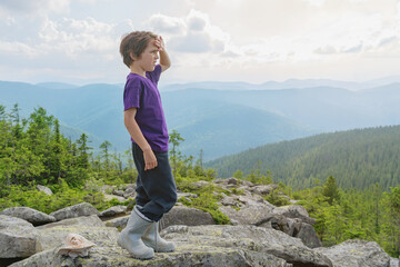 The boy is standing on top of a mountain. He looks at the scenery. Summer hiking.