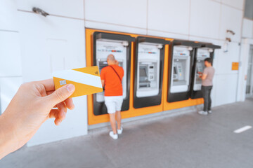 Hand holds a bank plastic card with a chip against the background of a number of ATMs in which customers withdraw or deposit money into the account