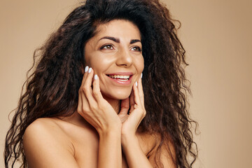 Smiling tanned awesome curly Latin lady using facial cream after 30s to keep skin collagen and...