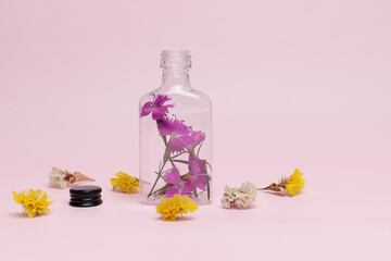 Obraz na płótnie Canvas Purple flowers in an open bottle, on a pale pink background. White and yellow dried flowers lie on the floor