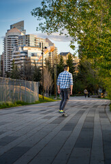 Fototapeta na wymiar Calgary Alberta Canada, May 16 2022: A young man rides a skateboard down a downtown walkway during a summer evening near Princess Island Park.
