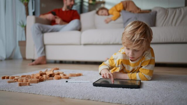 Little boy lying on floor and using tablet at home