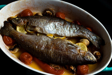 grilled trout in a blue baking dish, on a gray table surrounded by lemons, peppers, mushrooms and tomatoes, top view. The concept of healthy eating. Mediterranean recipe.