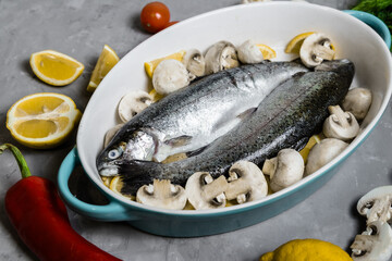 Raw trout in a blue baking dish, on a gray table surrounded by lemons, peppers, mushrooms and tomatoes, top view. Wild Fish, preparation for cooking. The concept of healthy eating. 
