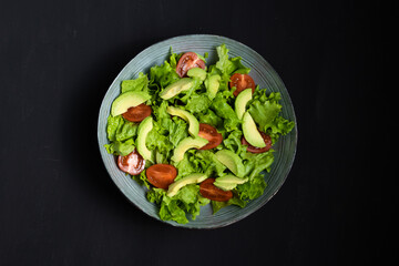 Green salad with avocado tomatoes, on a black background, top view. Healthy snack