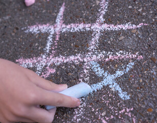 A close up image of a tic-tac-toe chalk game. Child is drawing on the ground background.