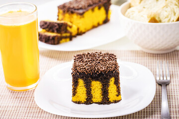 carrot cake with chocolate sprinkles, creamy frosting dripping down the cake, served with orange juice