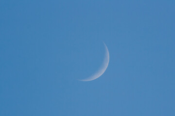 Waxing crescent moon against blue sky, 16% surface visible
