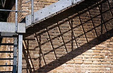 Schody przemysłowe ze stali ocynkowanej przymocowane do starej ściany z białej cegły. Cień stalowej konstrukcji na ścianie.