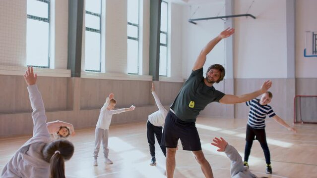 PE teachers and group of elementary students exercising during class at school gym.