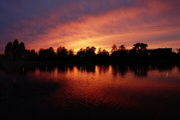 Obraz premium Sunset in orange tones with reflection in water and line of trees