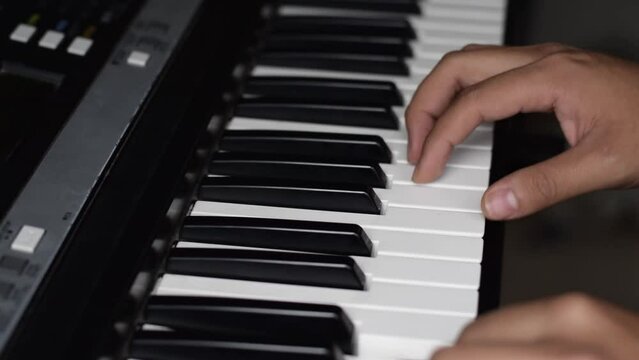 detail shot of a brunette boy's hands playing his synthesizer, practicing while watching online tutorials. young man improving his technique while playing the piano keys in his room.
