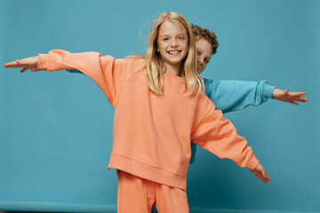 cute, beautiful, happy children a boy and a girl of school age stand on a blue background in bright plain clothes, facing the camera spreading their arms to the sides