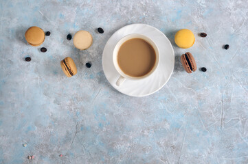 Fototapeta na wymiar White cup of coffee with cream with colorful french macaroons and coffee beans, on gray blue marble background, top view, copy space, selective focus on mug