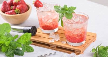 Cold summer strawberry cocktail mojito, margarita, daiquiri. Two glasses with fresh strawberry soda drink with ice cubes and mint leaves on light grey background. Iced strawberry lemonade, banner