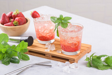 Cold summer strawberry cocktail mojito, margarita, daiquiri. Two glasses with fresh strawberry soda drink with ice cubes and mint leaves on light grey background. Iced strawberry lemonade, close up