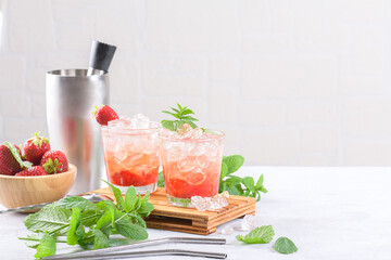 Cold summer strawberry cocktail mojito, margarita, daiquiri. Two glasses with fresh strawberry soda drink, ice cubes, mint and bartender tools on light background. Iced strawberry lemonade, copy space