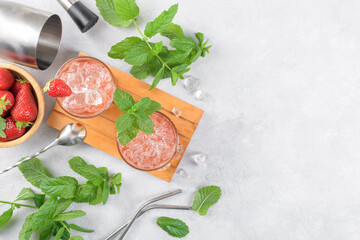 Cold summer strawberry cocktail mojito, margarita, daiquiri. Two glasses with fresh strawberry soda drink with ice cubes and mint leaves on light grey background. Iced strawberry lemonade, top view
