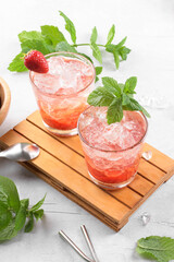 Cold summer strawberry cocktail mojito, margarita, daiquiri. Two glasses with fresh strawberry soda drink with ice cubes and mint leaves on light grey background. Iced strawberry lemonade, close up