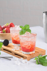 Cold summer strawberry iced cocktail mojito, margarita, daiquiri in two glasses with mint leaves on light background