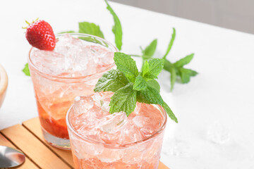 Cold summer strawberry cocktail mojito, margarita, daiquiri. Two glasses with fresh strawberry soda drink with ice cubes and mint leaves on light grey background. Iced strawberry lemonade, close up