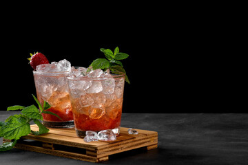 Cold summer strawberry cocktail mojito, margarita, daiquiri. Two glasses with fresh strawberry soda drink with ice cubes and mint leaves on dark background. Iced strawberry lemonade, copy space